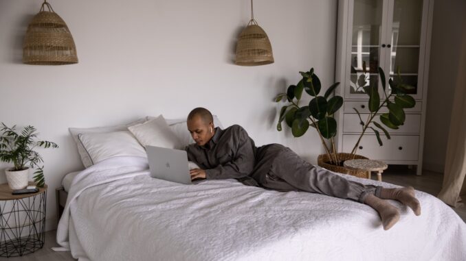 Mand ligger på seng med computer